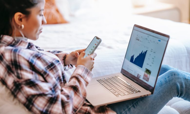 crop ethnic trader with smartphone and laptop on bench indoors