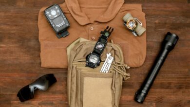 A brown polo on a wooden background with pieces of tactical gear on top, like a tactical bag, flashlight, and utility knife.