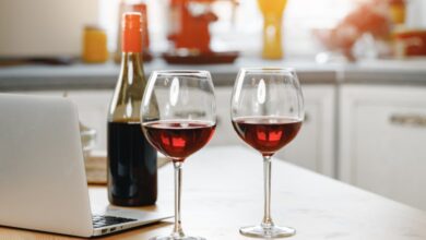 Two glasses of red wine, a half-full wine bottle, and a silver laptop sit on a kitchen island.