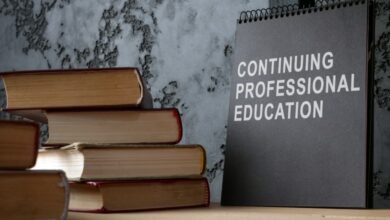 A notepad reading the words "Continuing Professional Education" sits next to several books stacked up on a desk.