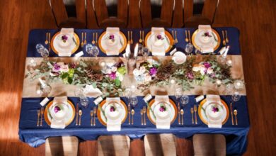 An overhead angle of a rectangular table. The table has a navy tablecloth, a beige runner, and gold chargers.