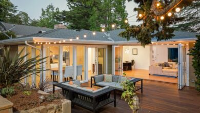 The patio of a modern home with hardwood floors, two loveseat sofas, string lights, and open foldable doors to the house.