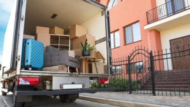 A truck packed with items is parked in front of a house. The truck is white and the house is made out of brick.