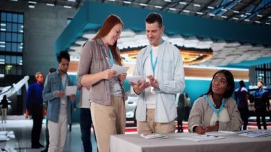 A man and woman standing outside a trade show booth at a conference while another woman sits beside them.