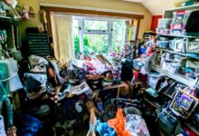 A cluttered room stacked floor to ceiling with hoarded items strewn about and a window letting in light on one end.