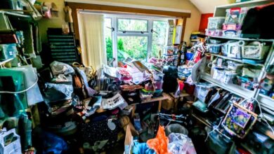 A cluttered room stacked floor to ceiling with hoarded items strewn about and a window letting in light on one end.